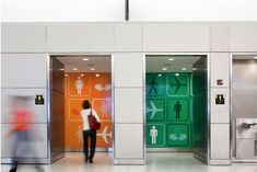 two people walking through an airport lobby with green and orange doors on either side of them