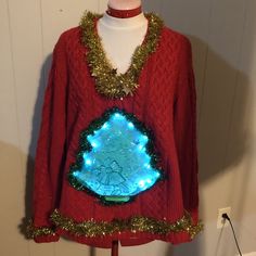 a red sweater with blue lights on it and a green tree in the center is hanging from a mannequin's head