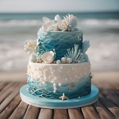 a three tiered blue and white cake sitting on top of a wooden table next to the ocean