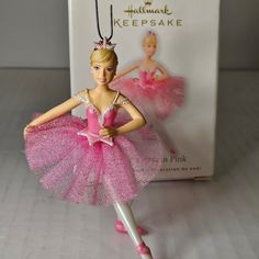 a pink ballerina ornament hanging from a string on a white background with a box