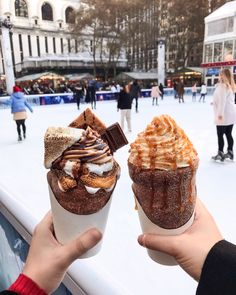 two people holding up ice cream and desserts in front of an outdoor skating rink