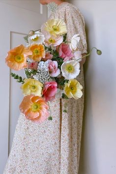 a woman in a long dress holding a bouquet of flowers next to a white door