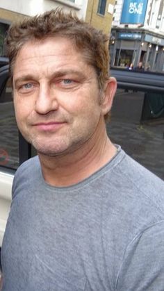 a man standing in front of a white car on a city street with buildings behind him