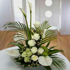 a vase with white flowers and greenery on a table