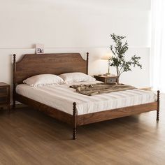 a bed sitting on top of a wooden floor next to a nightstand with a potted plant