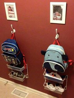 three backpacks hanging from hooks on a red wall with pictures and photos above them