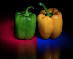 two green and yellow peppers sitting next to each other on a red and blue surface