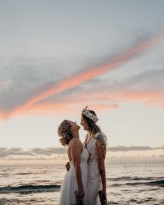 two women standing next to each other on the beach at sunset with clouds in the background