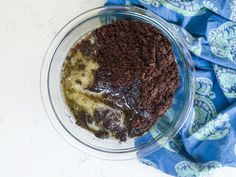 a glass bowl filled with brownie batter and other ingredients next to a blue towel