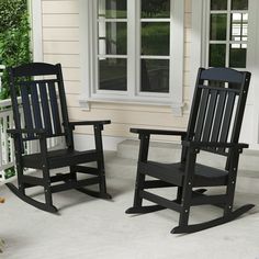 two black rocking chairs sitting in front of a house