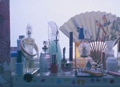 an assortment of perfumes and other items on a table with a fan in the background