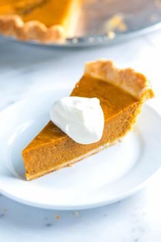 a slice of pumpkin pie on a white plate with a serving dish in the background