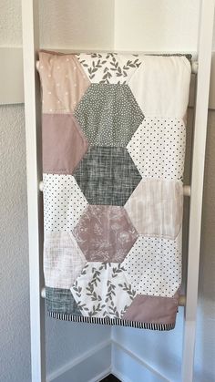 a quilt hanging from the side of a white ladder in a room with gray walls