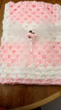 a pink and white crocheted blanket sitting on top of a wooden table