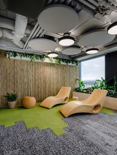 an office with green carpet and plants on the wall, two wooden lounge chairs in front of a window