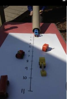 a child is playing with toy cars on a white table top near a wooden pole