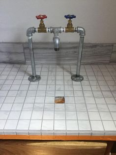 two faucets are connected to the floor in a bathroom with white tile and wood