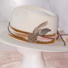 This hatband is gorgeous and has just a little extra added to it. The band is 22.5" x 1.5" and has adjustable ties in the back so it can fit hats from 22.5-34". The bottom layer is one of our favorite leathers, a metallic toasted bronze pink. Very subtle but gorgeous! The designer has then used two types of silk ribbons that complement the leather and really bring the color to life. The brown suede lace adds a nice complete to complete the top layer. As if that wasn't enough...we have added a sm Adjustable Fedora Hat Bands For Rodeo, Spring Adjustable Top Hat With Flat Crown, Fitted Hat Band For Kentucky Derby With Flat Crown, Adjustable Flat Crown Hat For Fall, Spring Adjustable Flat Crown Top Hat, Kentucky Derby Hats With Flat Crown For Country Events, Adjustable Wide Brim Top Hat For Ranch, Adjustable Cream Felt Hat With Flat Crown, Adjustable Flat Brim Hat Band For Rodeo