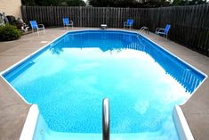 an empty swimming pool with blue chairs and a fence in the backround behind it