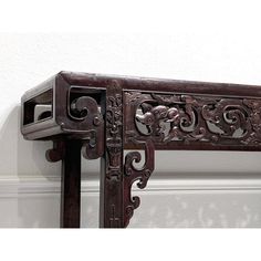 an ornate wooden shelf with carvings on the top and bottom, against a white wall