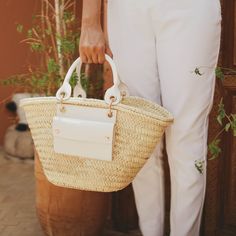 Handmade by craftswomen from our rural cooperative DOUM FOR WOMEN, our totes are made with impeccable craftsmanship and from high quality materials. Basket carryall bag as the perfect summer staple. Fresh, light and versatile tote with a rather rustic feel and a market vibe, ideal for strolling around in style from the beach to the city. This handwoven basket crafted from palm leaves is enriched with high-end classic vegan leather details, an exterior pocket and a removable canvas pouch with a z Luxury Straw Bucket Bag For Daily Use, Luxury Summer Bags With Bamboo Handle, Luxury Summer Bag With Bamboo Handle, Luxury Casual Straw Beach Bag, Luxury Chic Straw Bag For Everyday Use, Luxury Beach Bucket Bag In Natural Fiber, Luxury Straw Bag For Vacation, Luxury Square Straw Travel Bag, Luxury Summer Bags For Everyday Use