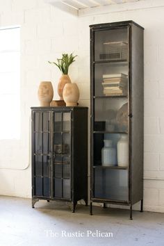 two vases are sitting on top of an old metal and glass cabinet in a white room