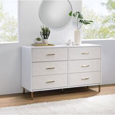 a white dresser with two plants and a round mirror