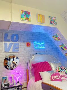 a bedroom with white brick walls and colorful lights on the wall above the bed is decorated with pink, blue, and red pillows