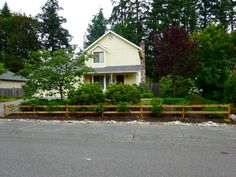 a yellow house sitting on the side of a road next to a lush green forest