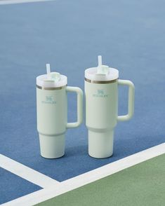 two white coffee mugs sitting on top of a tennis court