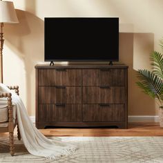 a flat screen tv sitting on top of a wooden dresser in a living room next to a lamp