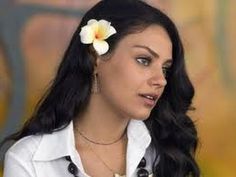 a woman with a flower in her hair looking off to the side while wearing a white shirt