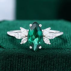 an emerald colored ring with two white diamonds on the top and one green stone in the middle