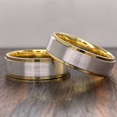 two gold and silver wedding bands on top of a wooden table next to each other