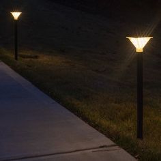 three lights that are sitting on the side of a sidewalk in the grass at night