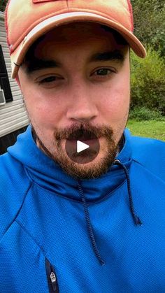 a man with a beard wearing a baseball cap and making a funny face at the camera