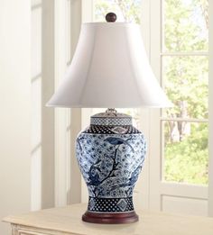 a blue and white vase sitting on top of a wooden table next to a lamp