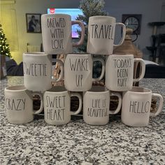 twelve coffee mugs with words written on them sitting on a counter in front of a television