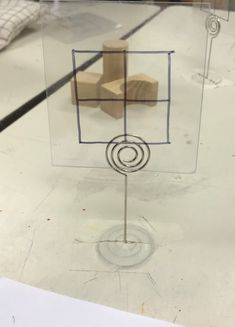 a glass display case with a wooden block and metal wire in the shape of a square