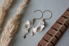 two pairs of earrings sitting on top of a table next to some dried grass and feathers