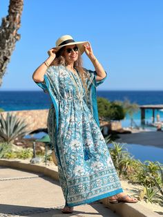 Our Aegean Blue Floral Maxi is an all over floral kaftan dress that is the perfect piece to dress up and wear out, wear to the beach as a cover-up, or just lounge about in it at home! This beautiful dress is named after none other than the aegean blue sea, which boasts the most gorgeous blue/teal colouring! Subtle variations in colour and pattern are to be celebrated as they are evidence of the hand made block printing and dyeing process that makes this dress unique. This dress is the epitome of classic comfort and is perfect to use spring, summer, and into early fall. It is also available in midi and short lengths. One size with drawstring waist Length is 54" 100% cotton voile Made in India Machine wash delicate cold in a lingerie bag to protect tassels or hand wash. Hang dry. Blue V-neck Maxi Dress For Poolside, Blue Boho Dress For Beach Cover-up, Blue Maxi Length Poolside Cover-up, Turquoise V-neck Maxi Dress For Vacation, Resort Beach Cover-up Kaftan In Maxi Length, Resort Beach Cover-up Kaftan Maxi Length, Resort Beach Cover-up Maxi Length Kaftan, Resort Beach Cover-up Maxi Kaftan, Bohemian V-neck Maxi Dress For Resort