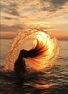 a woman standing in the water with her hair blowing back into the air at sunset