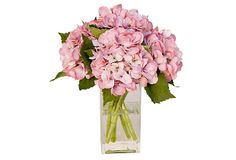 a clear vase filled with pink flowers on top of a white table next to green leaves