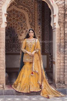 a woman in a yellow lehenga standing outside an archway with her hands on her hips