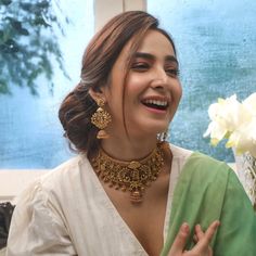 a woman in a green and white sari smiles as she holds her hand up to her chest