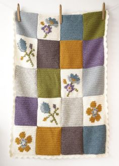 a crocheted blanket with flowers on it hanging from a clothes pegs holder