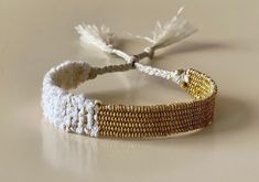 a white and gold beaded bracelet with tassels sits on a beige surface