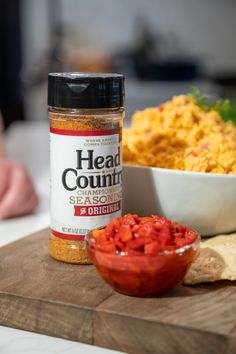 a wooden cutting board topped with a bowl of food and a jar of seasoning