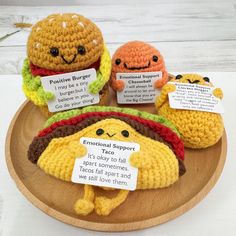 three crocheted hot dogs on a plate with labels attached to the buns