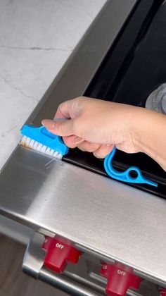 a person holding a toothbrush in front of an oven with red knobs on it